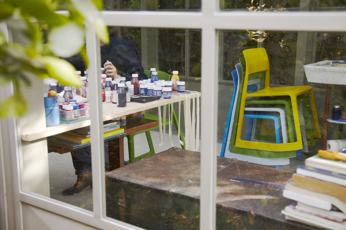 Gestapelte Vitra Tip Ton Stühle aus Kunststoff in Gelb, Grün, Weiß und Blau hinter Fenster.