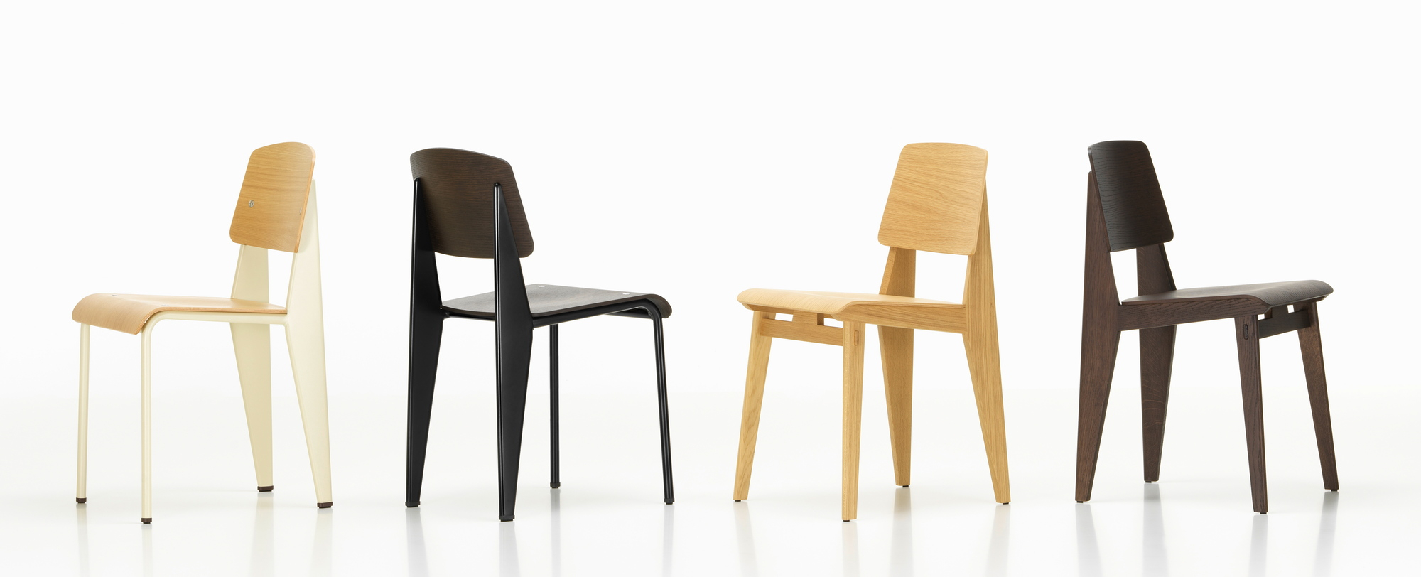 Vier Vitra Chaise Tout Bois Stühle aus Holz in verschiedenen Farben vor weißem Hintergrund.