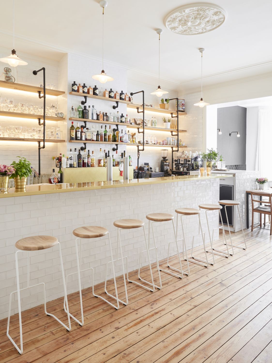 Reihe von Extremis Tiki Hockern mit Holzsitzen und weißen Metallgestellen vor einer Bar.