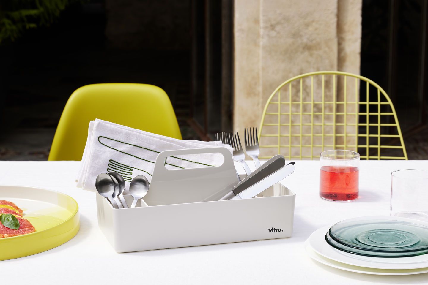 Esstisch-Szene mit Vitra Toolbox, Geschirr und zwei Stühlen, darunter ein gelber Eames Plastic Side Chair DSR.
