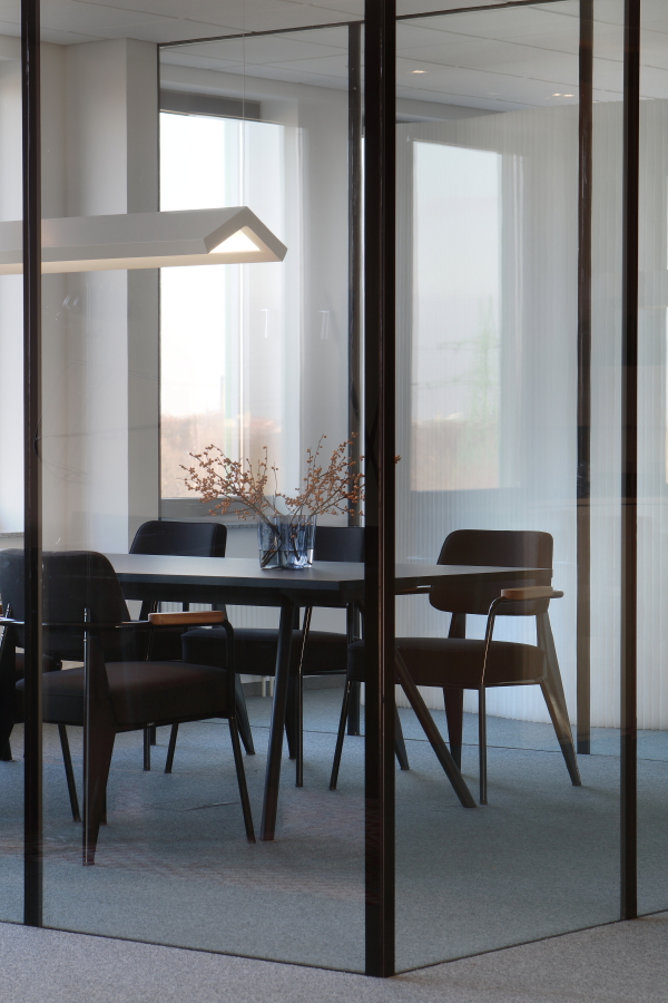 Moderner Konferenztisch mit Stühlen in einem Büro mit Glaswänden und minimalistischer Pendelleuchte.