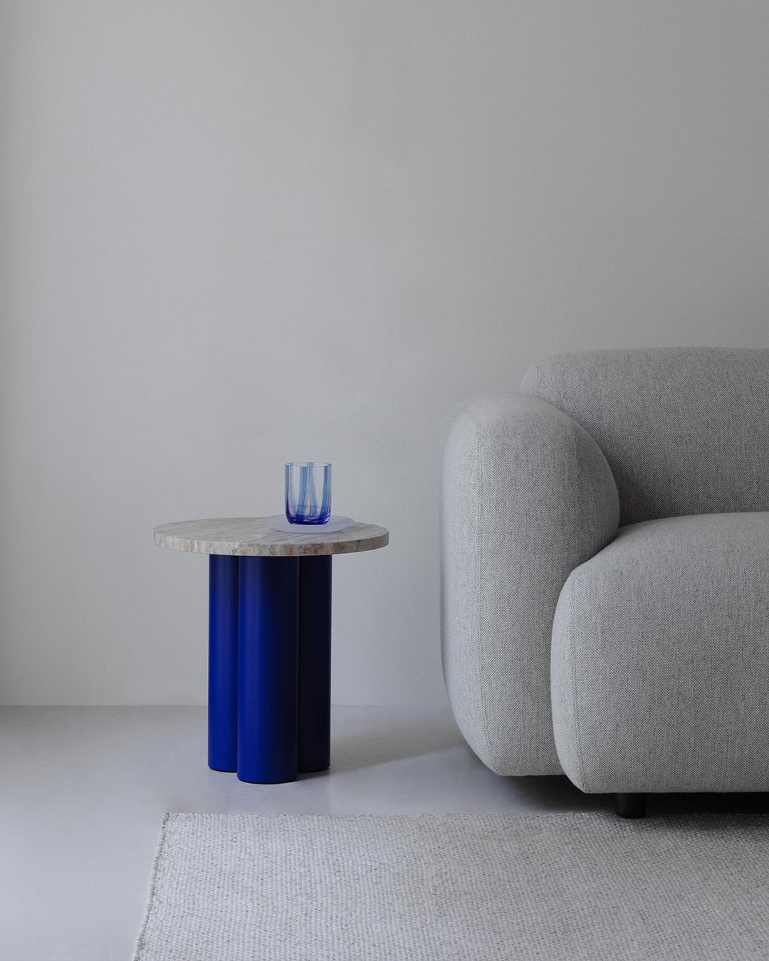 Normann Copenhagen Dit Coffee Table Beistelltisch mit blauen Beinen und Marmorplatte neben einem Sofa.