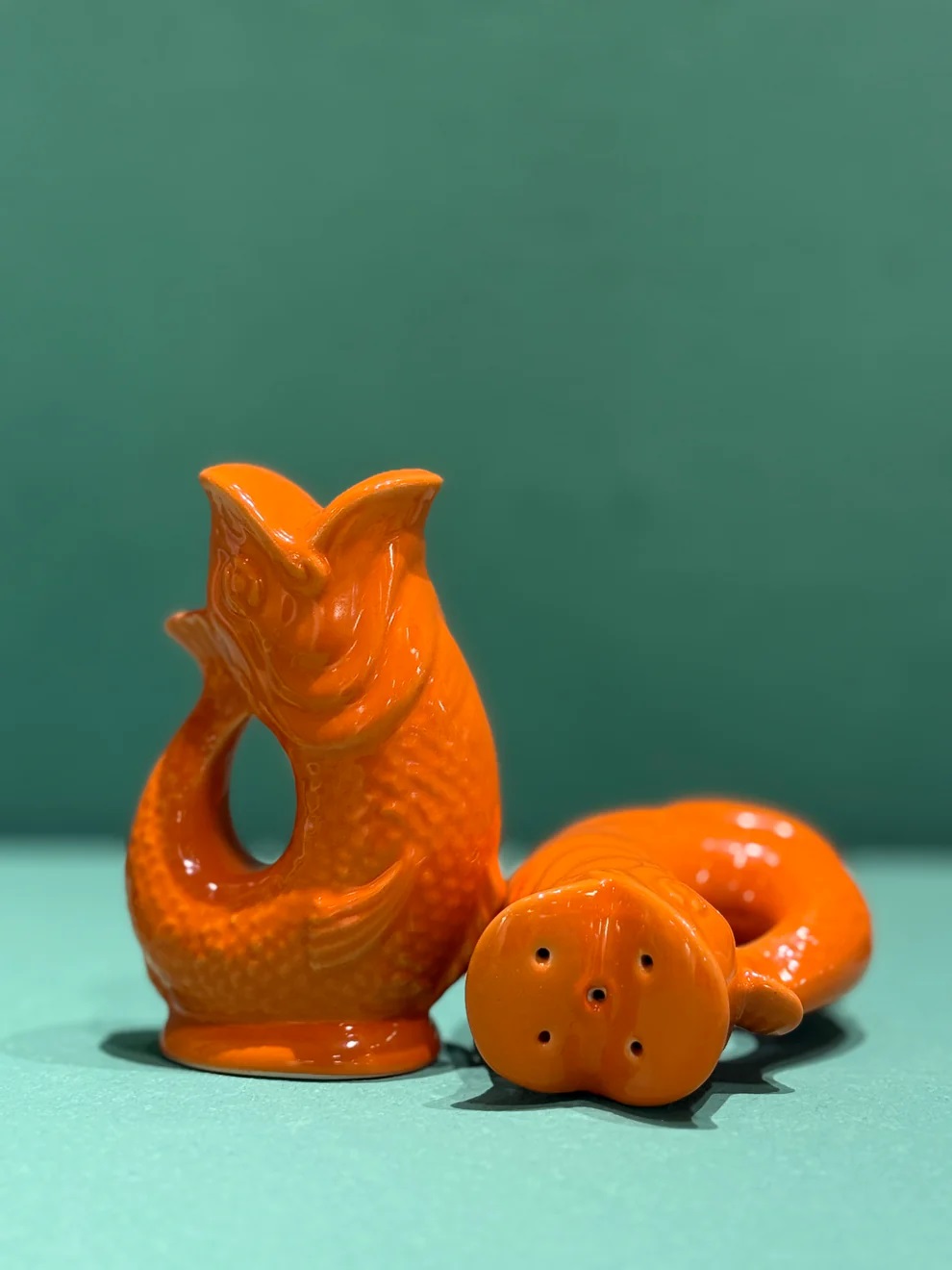 Orangefarbene Gluggle Fisch Salz- und Pfefferstreuer Set, einer steht, einer liegt, Nahaufnahme.