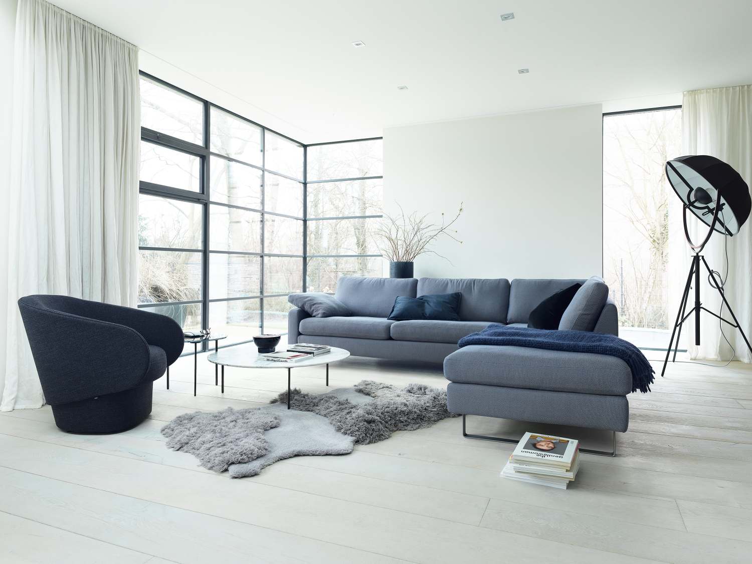 Helles Wohnzimmer mit grauem Conseta Sofa, Sessel, Couchtisch und Tageslicht für modernes Wohnen.