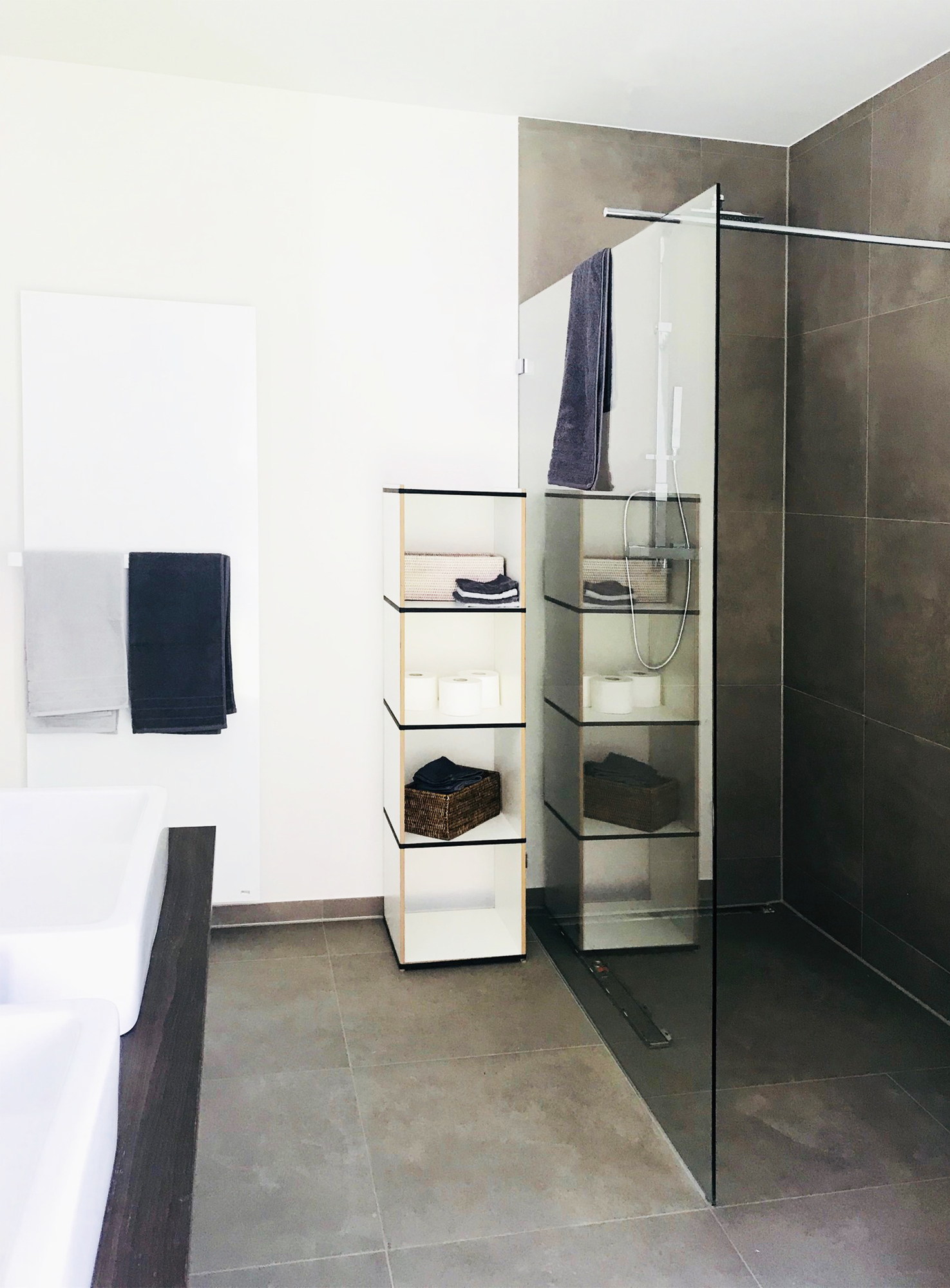 Badezimmer mit Tojo Regal Modul, weißem Waschtisch, Handtüchern und ebenerdiger Dusche für modernes Interior Design.