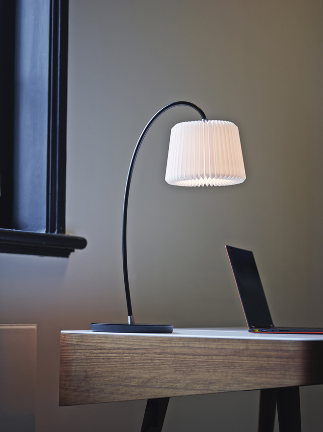 Snowdrop Tischleuchte von Le Klint auf einem Schreibtisch, mit plissiertem Lampenschirm und modernem Design.