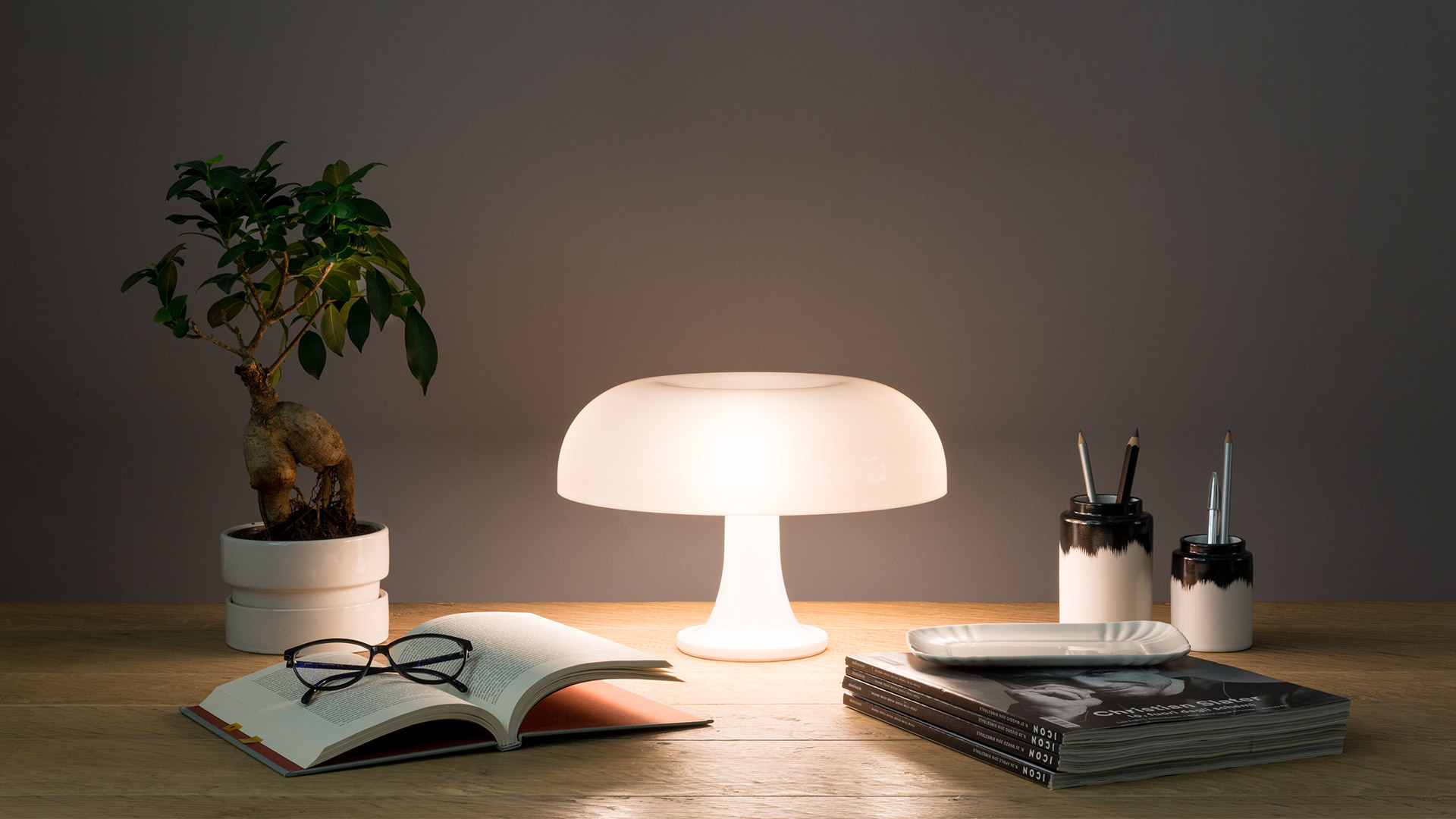 Nessino Tischleuchte von Artemide, pilzförmige Designerlampe auf einem Schreibtisch mit Deko-Elementen.