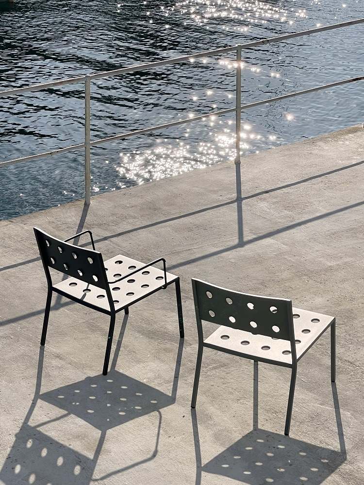 Zwei Hay Balcony Outdoor Lounge Chairs aus Metall mit runden Aussparungen vor Wasser.