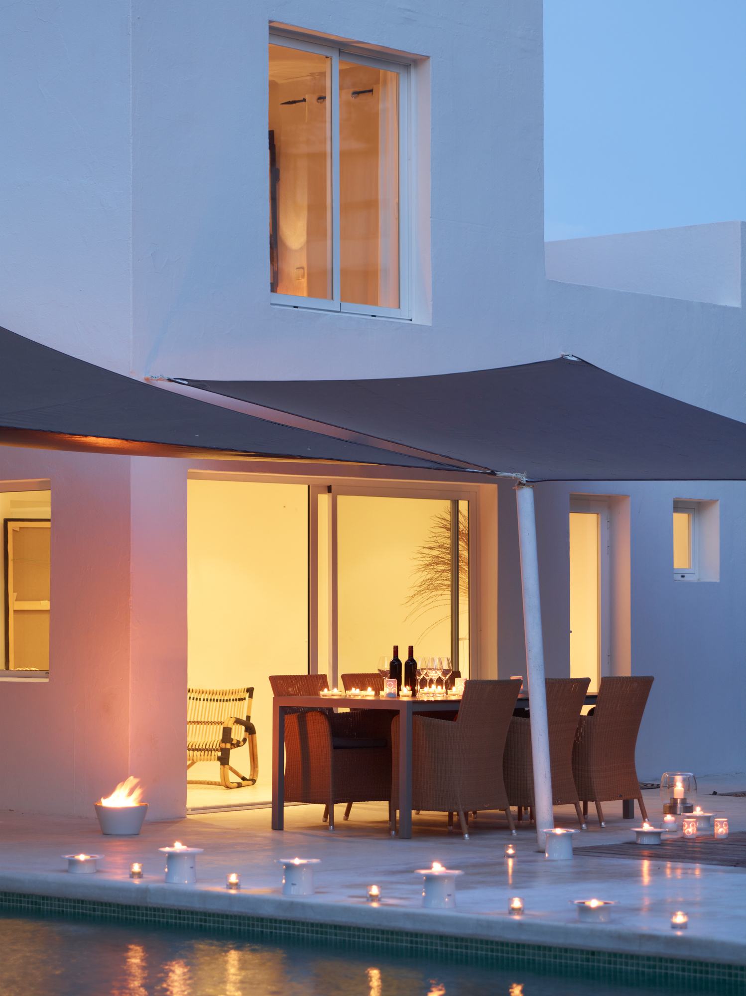 Hampsted Cane-Line Outdoor Sessel aus Rattan auf Terrasse mit Esstisch und Pool bei Nacht.