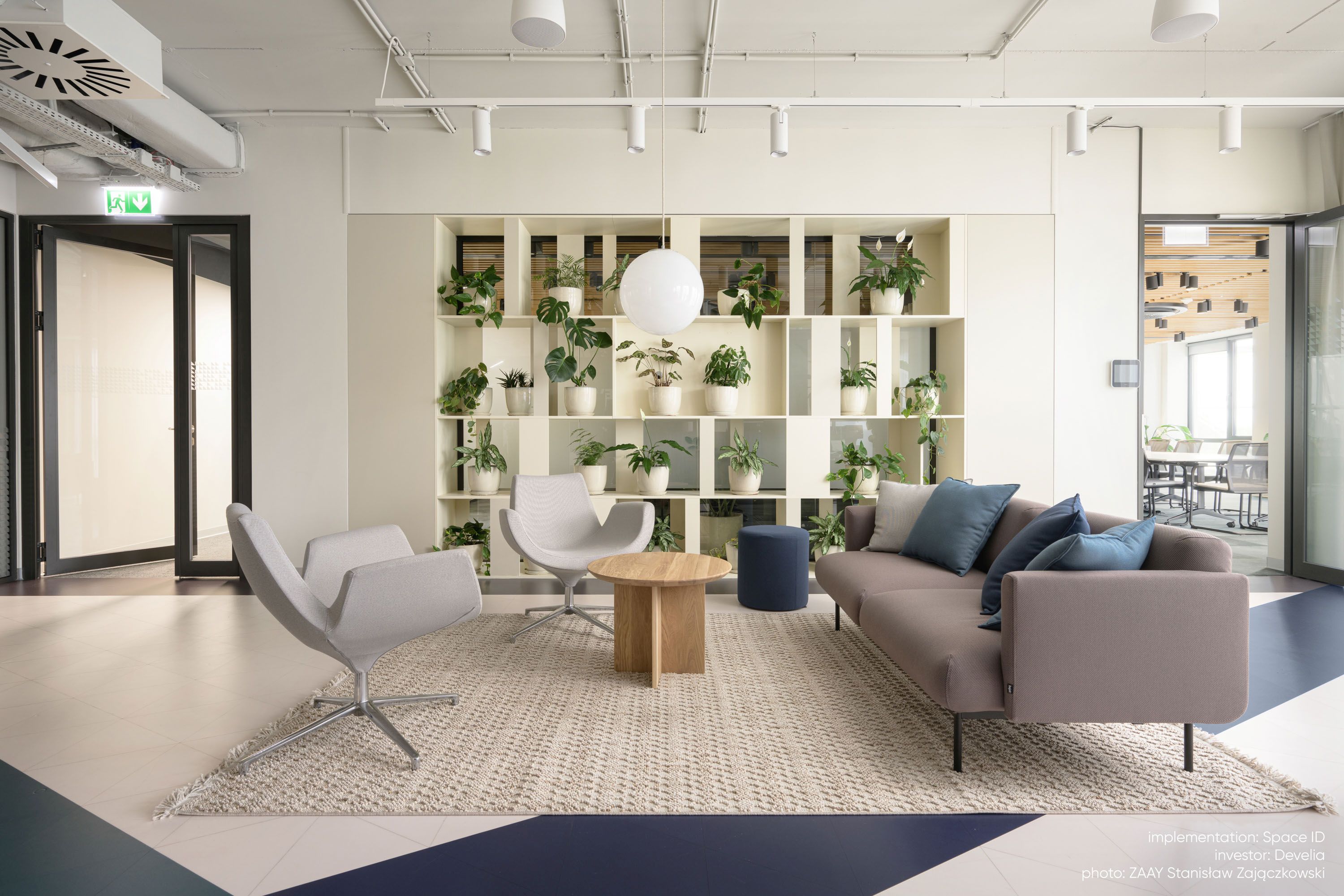 Modernes Büro-Interieur mit fora FR 422 Sofa 2-Sitzer Bejot in Grau, Sesseln, Holztisch und Pflanzenregal.
