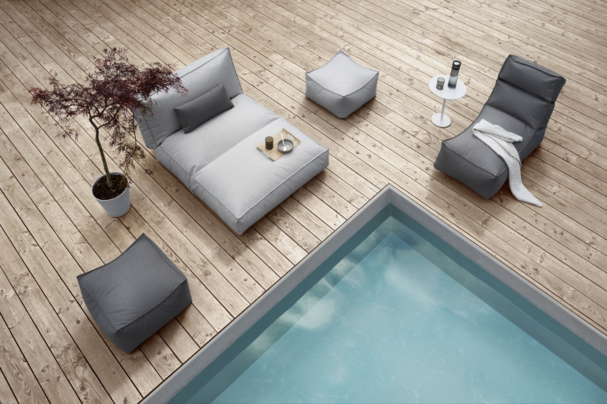 Außenbereich mit Blomus STAY Kissen in Grau und Beige, Liege, Poufs und Pool.