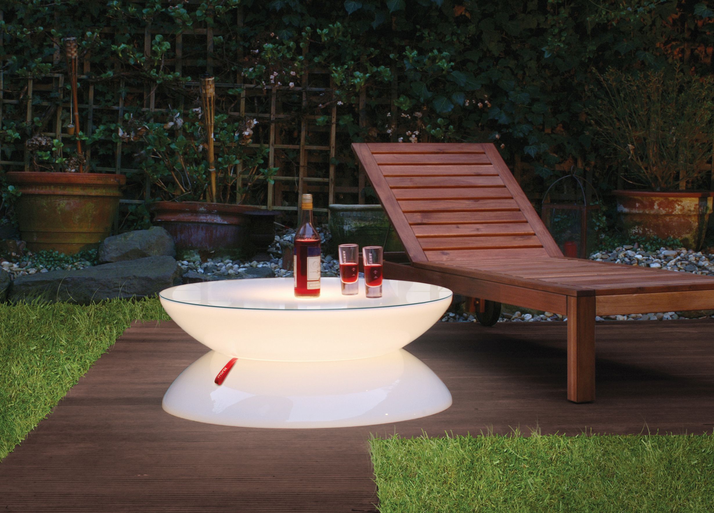 Moree Lounge Tisch, beleuchtet, mit Getränken auf einer Holzterrasse neben einer Sonnenliege.