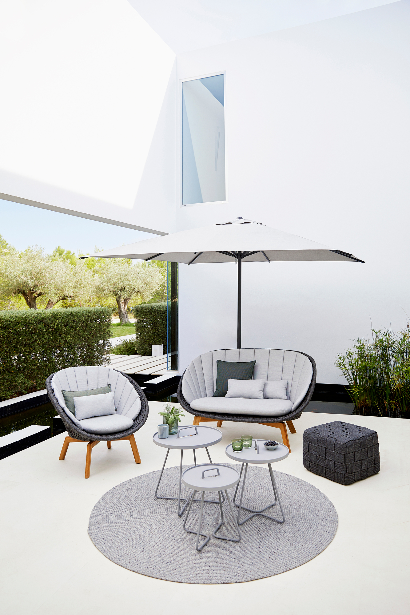 Peacock Outdoor Sofa von Cane-Line, 2-Sitzer mit Geflecht, Sessel, Beistelltische und Sonnenschirm.
