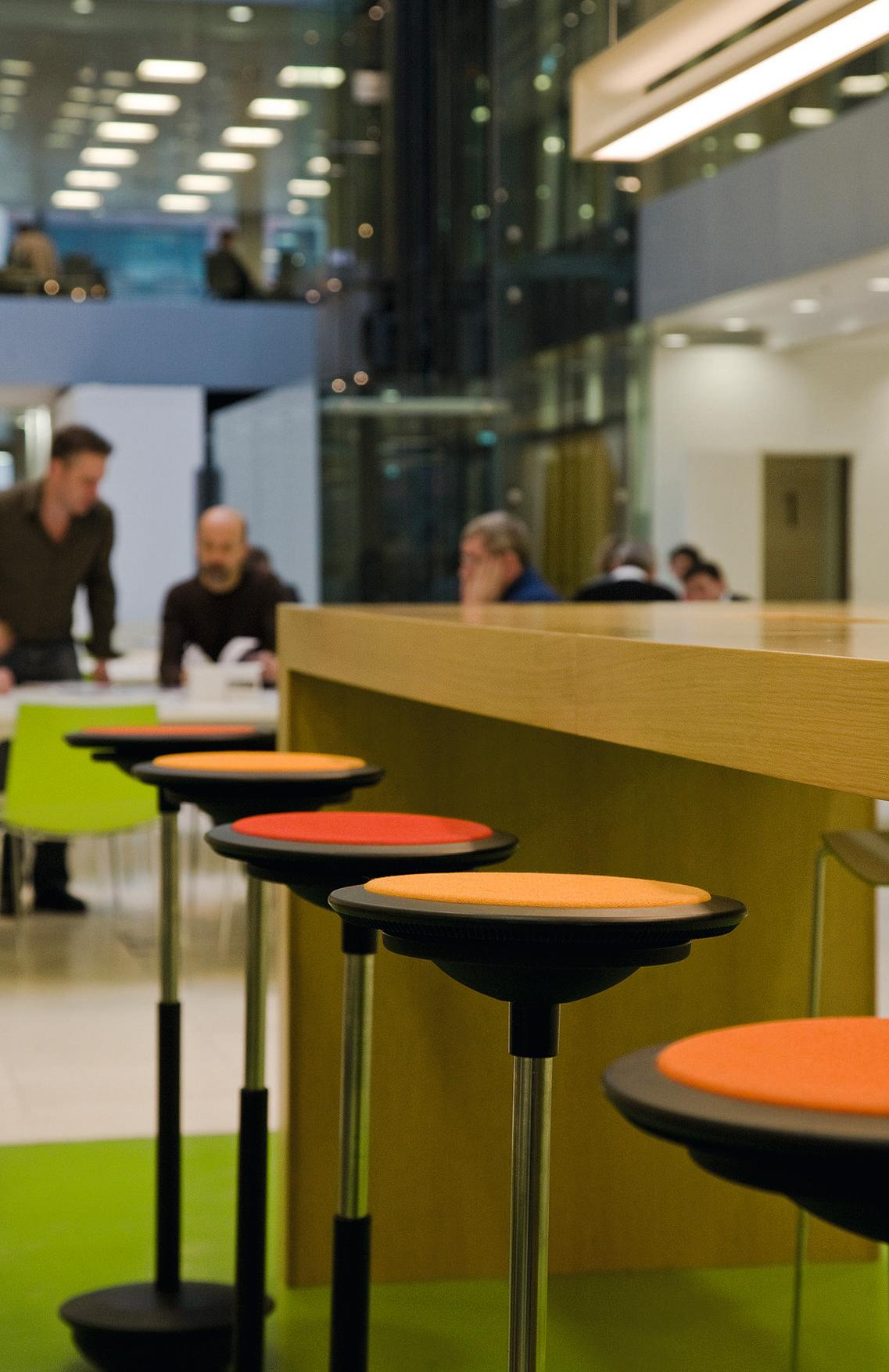Wilkhahn Stitz Stehhocker in Orange und Rot vor einer Theke in einem Büro.