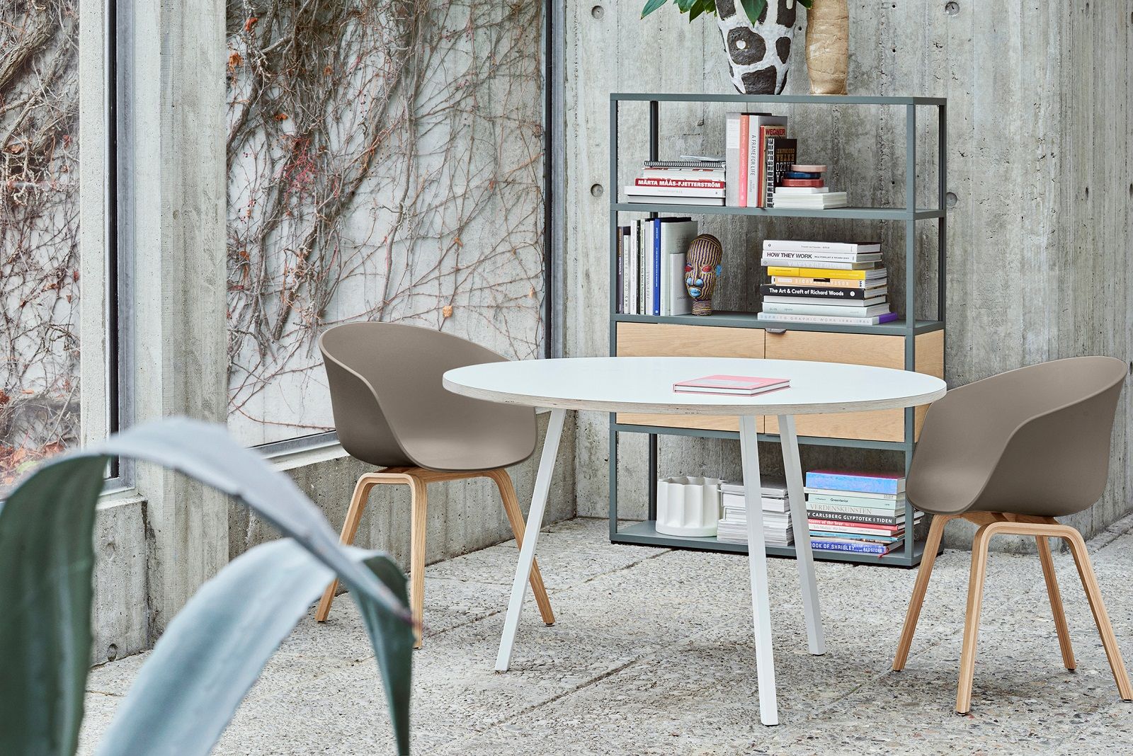 Heller Raum mit Hay Loop Stand Table Round Esstisch, Stühlen und Regal mit Büchern.