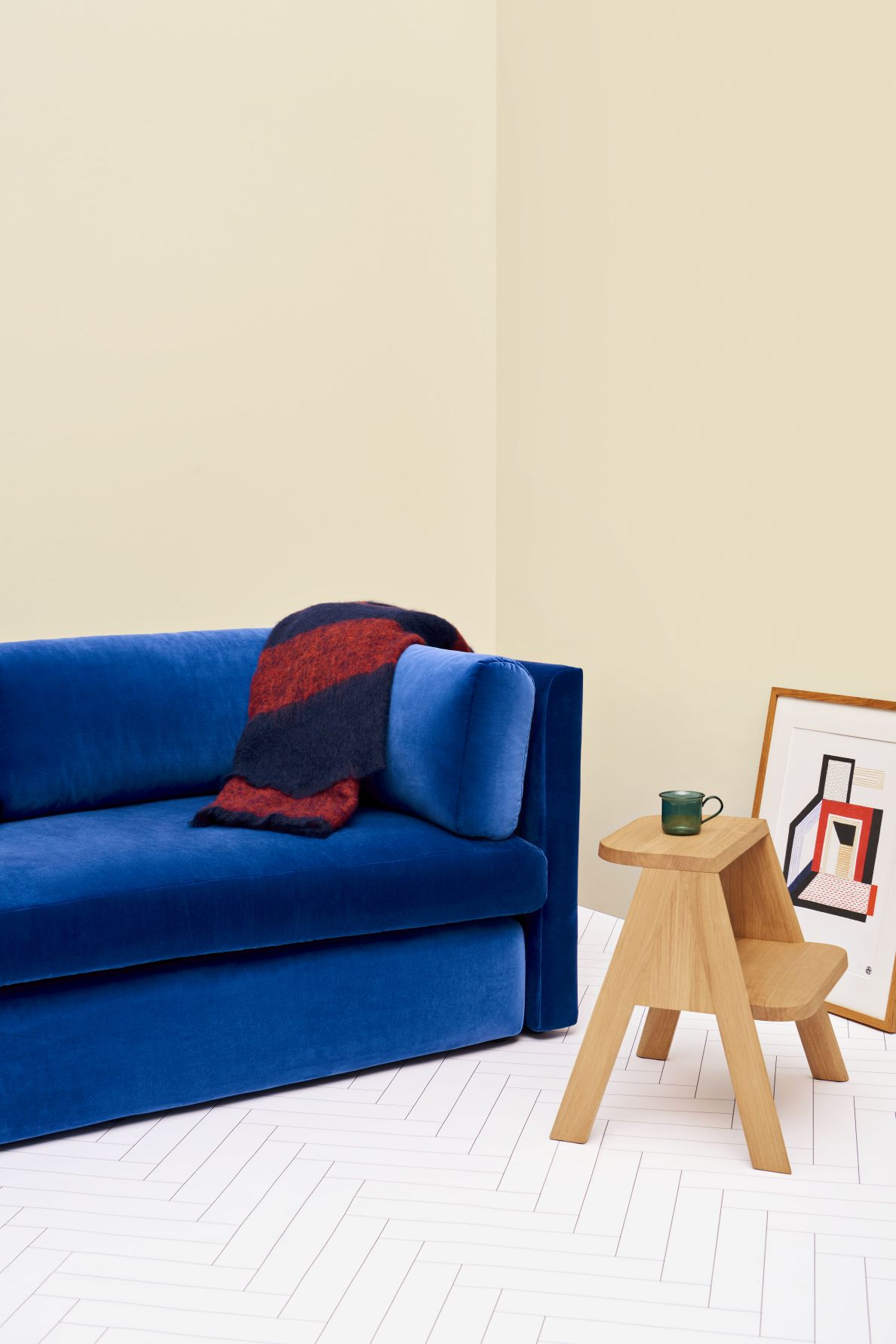 Hay Butler Hocker aus Eiche neben blauem Sofa mit Decke und gerahmtem Bild.
