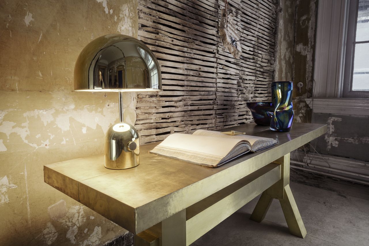 Goldene Bell Tischleuchte von Tom Dixon auf einem Schreibtisch mit Buch und Dekoration.