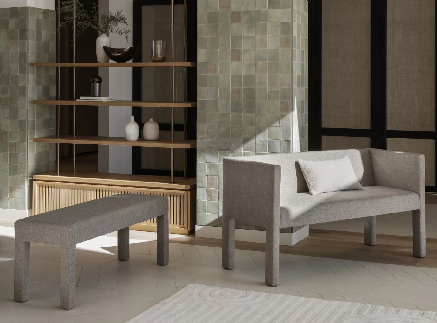 Blomus Sitta Sofa und Hocker in grauem Stoffbezug vor Regal und Fliesenwand.