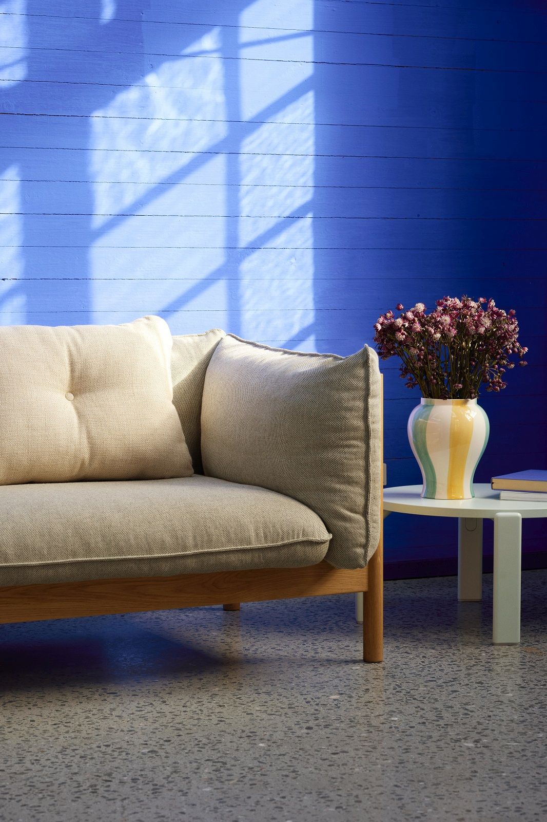 Nahaufnahme des Arbour Eco Sofa 2-Sitzer von Hay mit hellbeigen Kissen und Holzelementen neben einem Beistelltisch.
