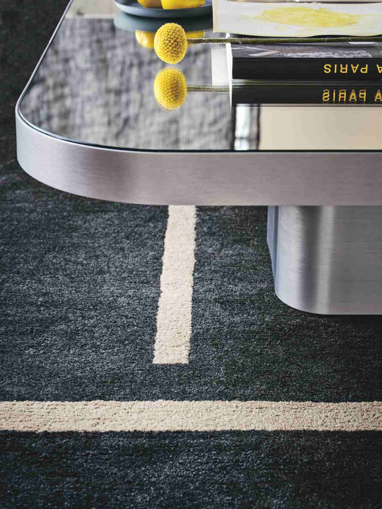 Detailaufnahme des ClassiCon Bow Coffee Table No. 2 mit Glasplatte und silbernem Fuß auf Teppich.