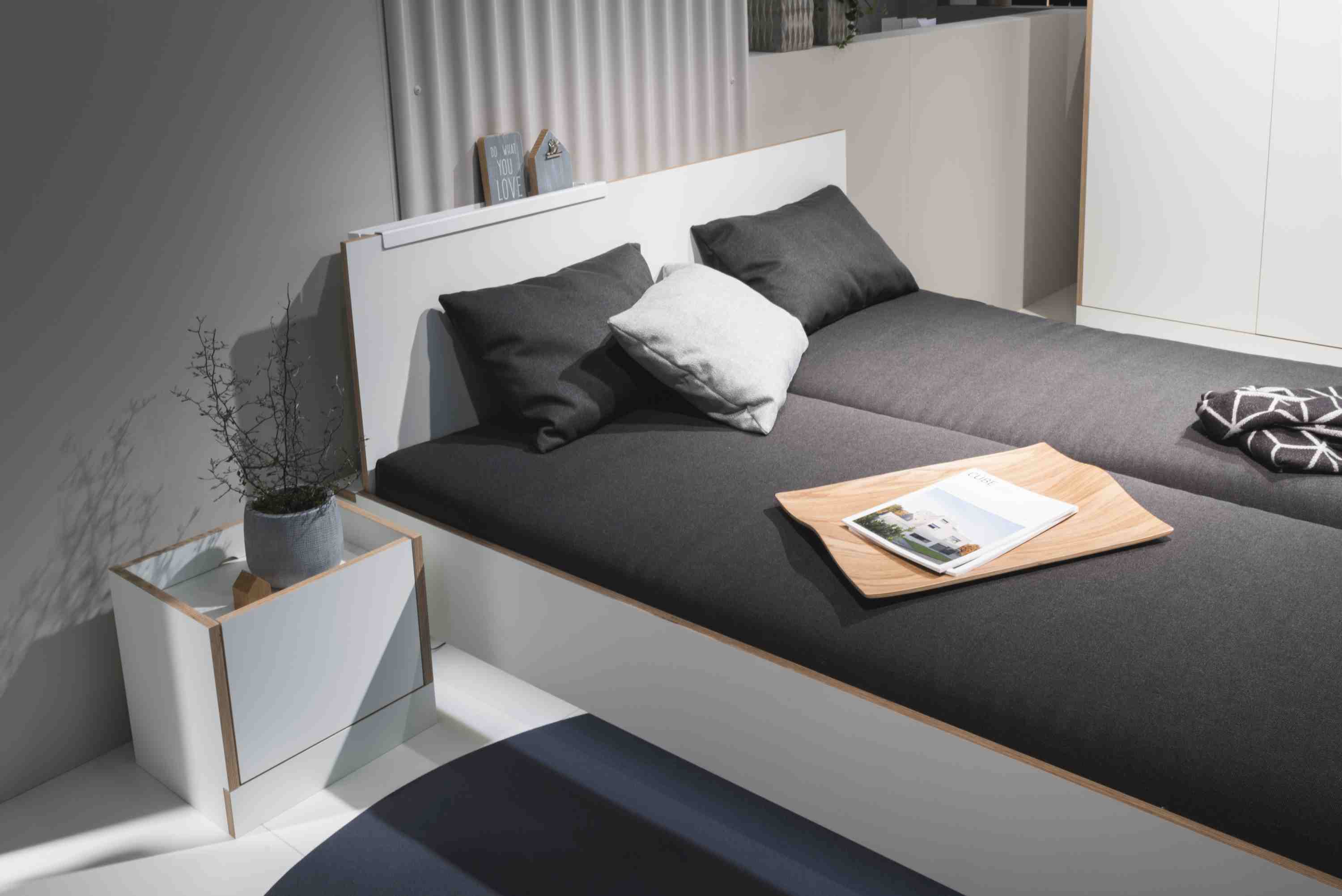 Weißes Flai Bett von Müller Möbelwerkstätten mit grauer Matratze und Nachttisch. Modernes Schlafzimmer Design.