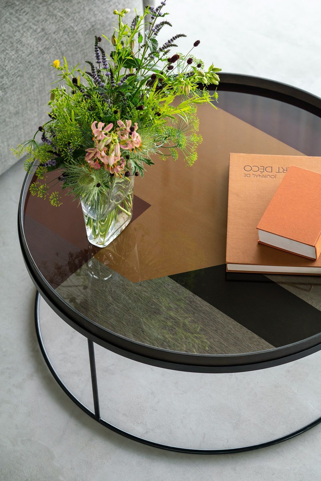 Ethnicraft Couchtisch mit Blumenstrauß und Büchern, runder Wohnzimmertisch mit Glasplatte und Metallgestell.