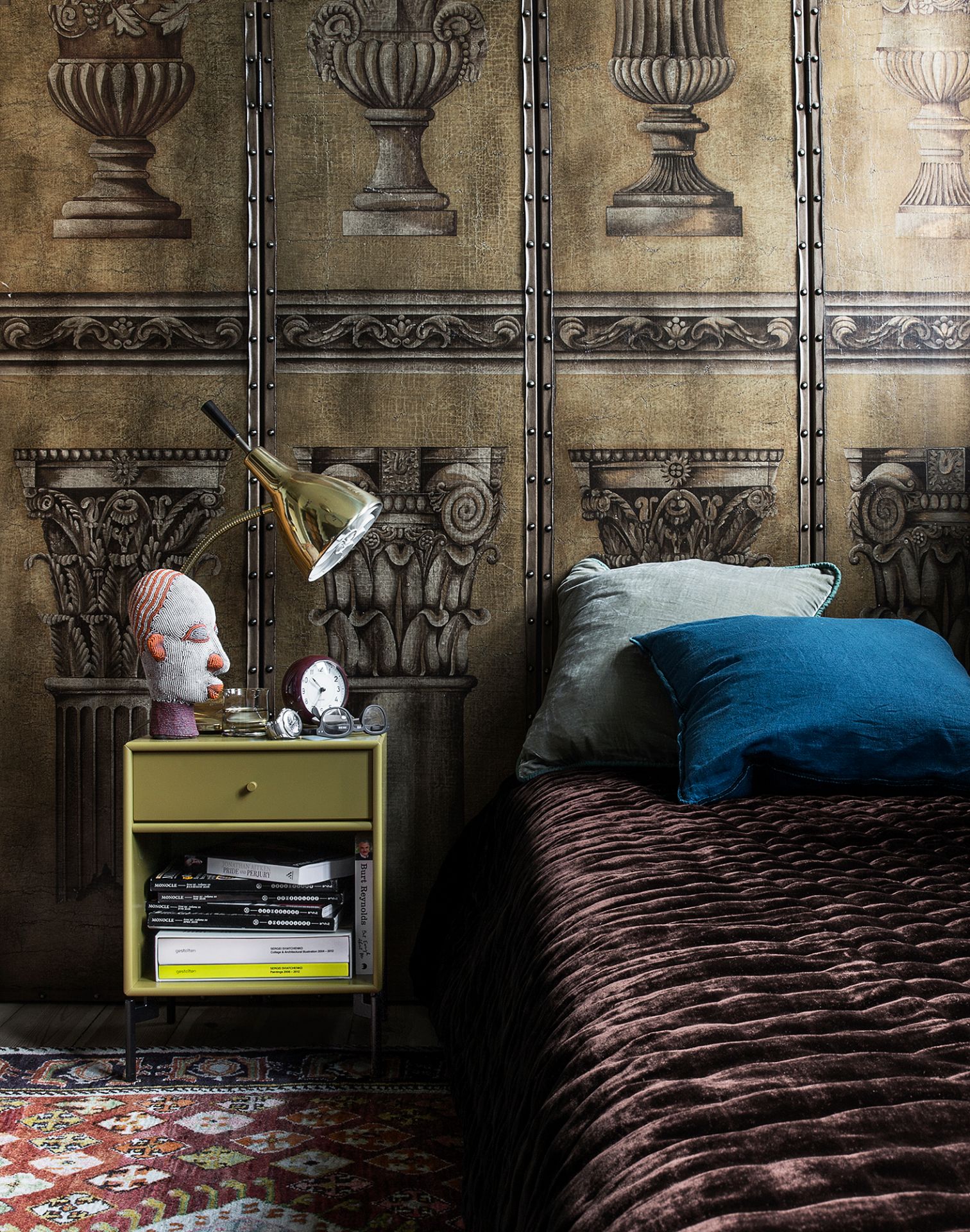 Schlafzimmer Interieur mit brauner Tagesdecke, blauen Kissen und gelbem Nachttisch mit Lampe und Deko.