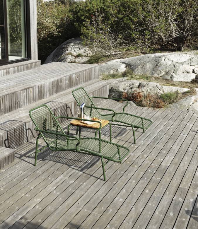 Zwei grüne Normann Copenhagen Vig Chaise Longue Liegen mit kleinem Tisch auf einer Holzterrasse.