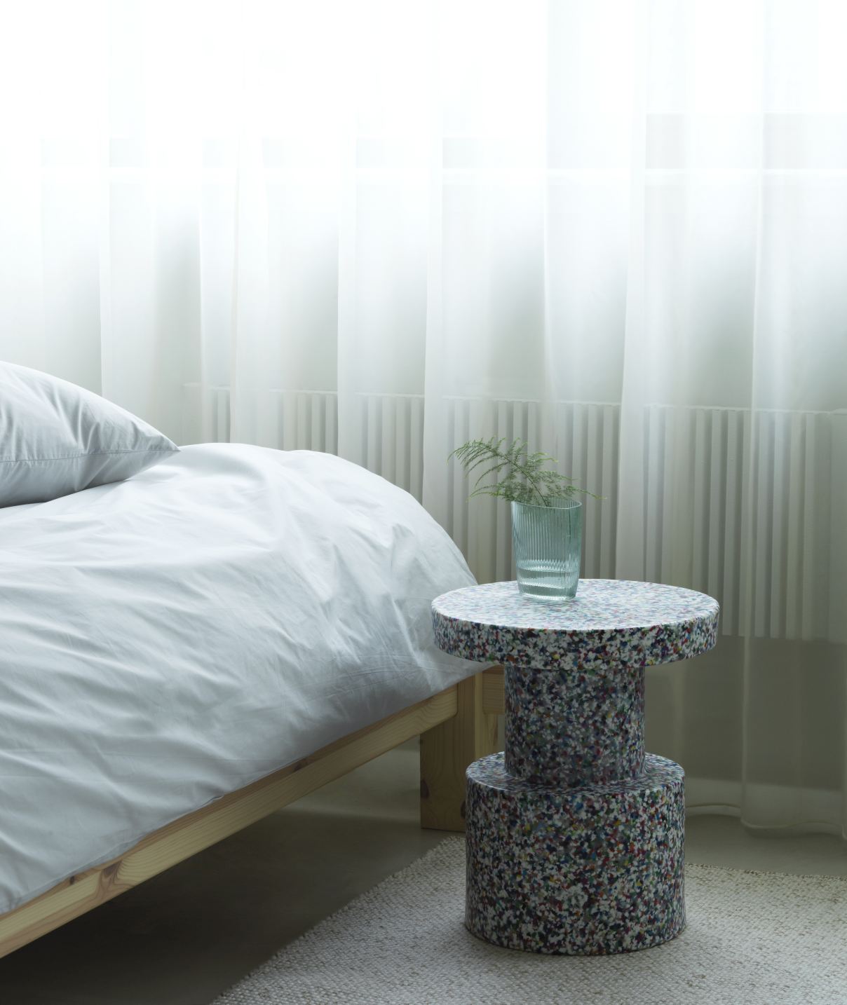 Normann Copenhagen Bit Stool Hocker aus recyceltem Kunststoff neben einem Bett mit weißer Bettwäsche.