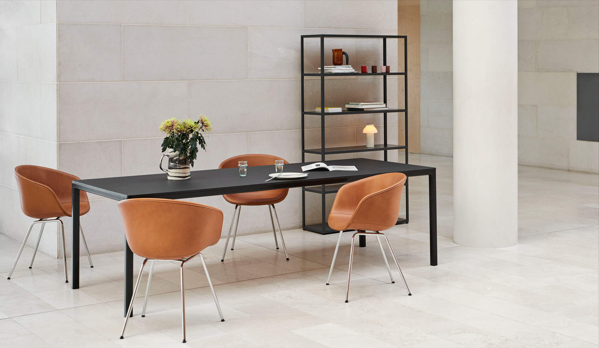 Esszimmer-Szene mit vier About A Chair AAC27 Stühlen in braunem Leder um einen schwarzen Esstisch.
