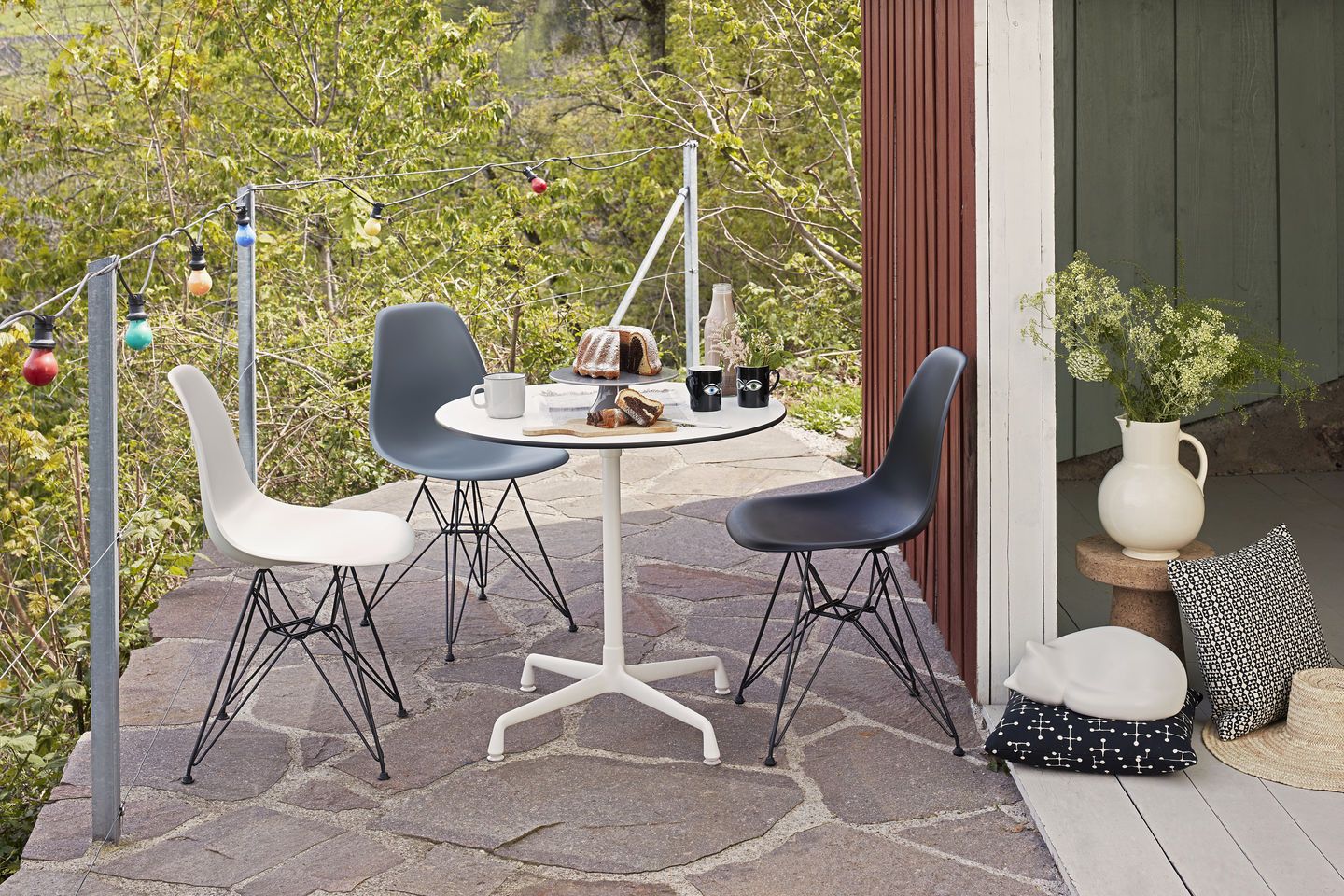 Drei Vitra Eames Stühle in Weiß, Grau und Schwarz um einen Gartentisch auf einer Terrasse.
