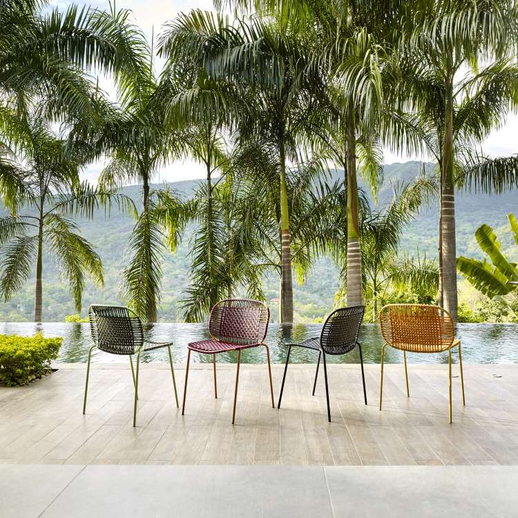 Vier farbige Cielo Stühle von ames, stapelbare Outdoor-Stühle vor Pool und Palmen.
