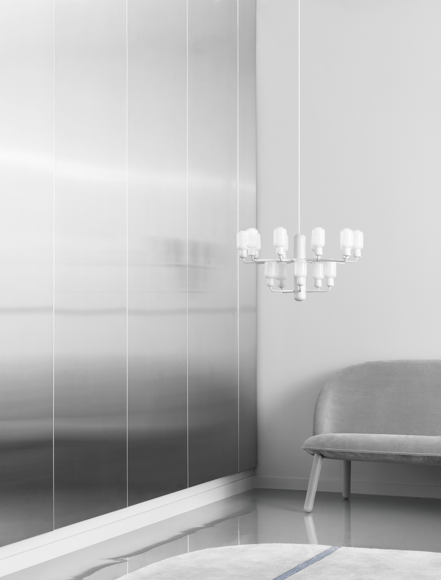 Weiße Amp Chandelier Pendelleuchte Small im minimalistischen Raum mit Sofa und silberner Wand.