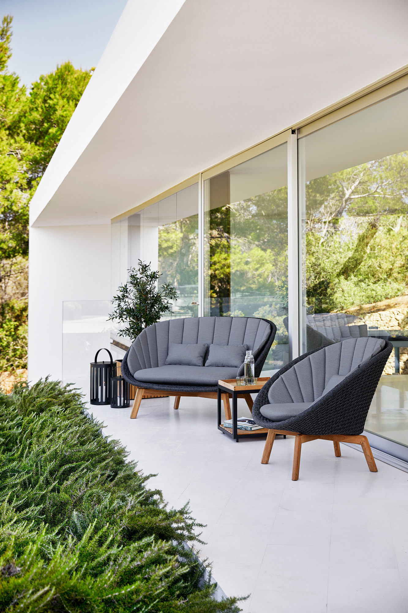 Graues Cane-Line Peacock Outdoor Sofa und Sessel auf einer Terrasse mit Tisch und Dekoration.