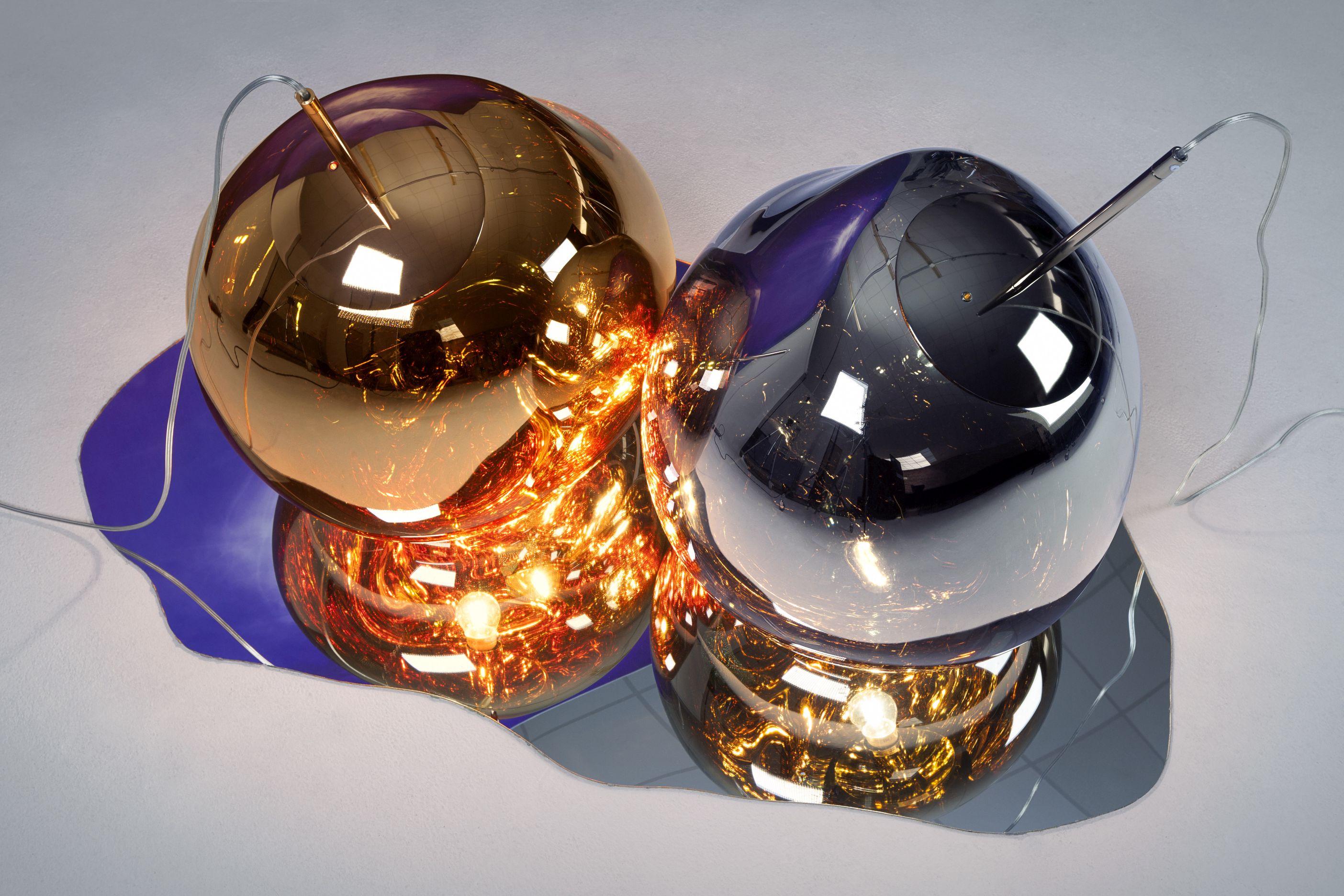 Nahaufnahme von zwei Tom Dixon Melt LED Pendelleuchten in Gold und Chrom mit warmem Licht.