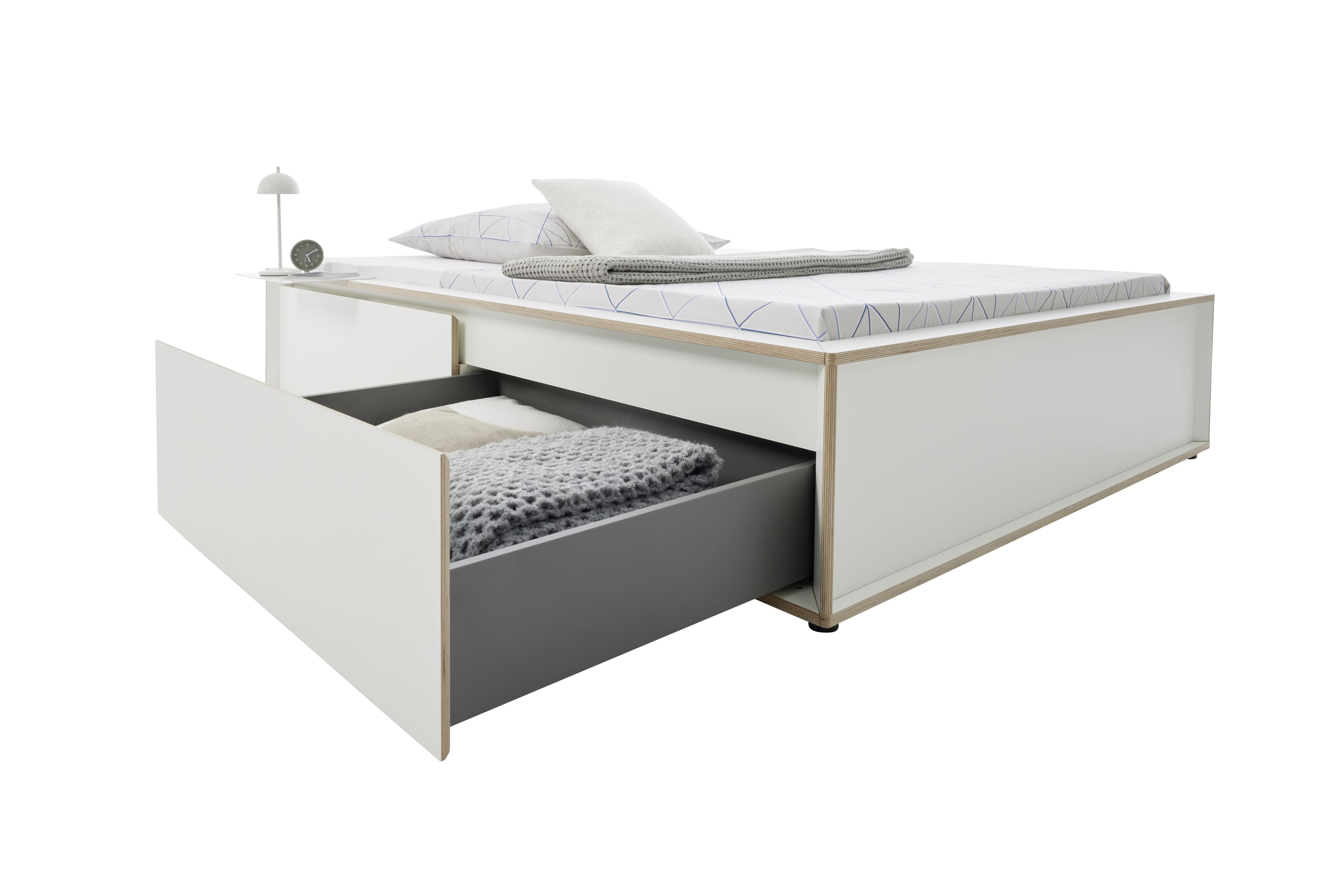 Spaze Bett von Müller Möbelwerkstätten mit Schublade, Nachttisch, Lampe, Kissen und Decke.