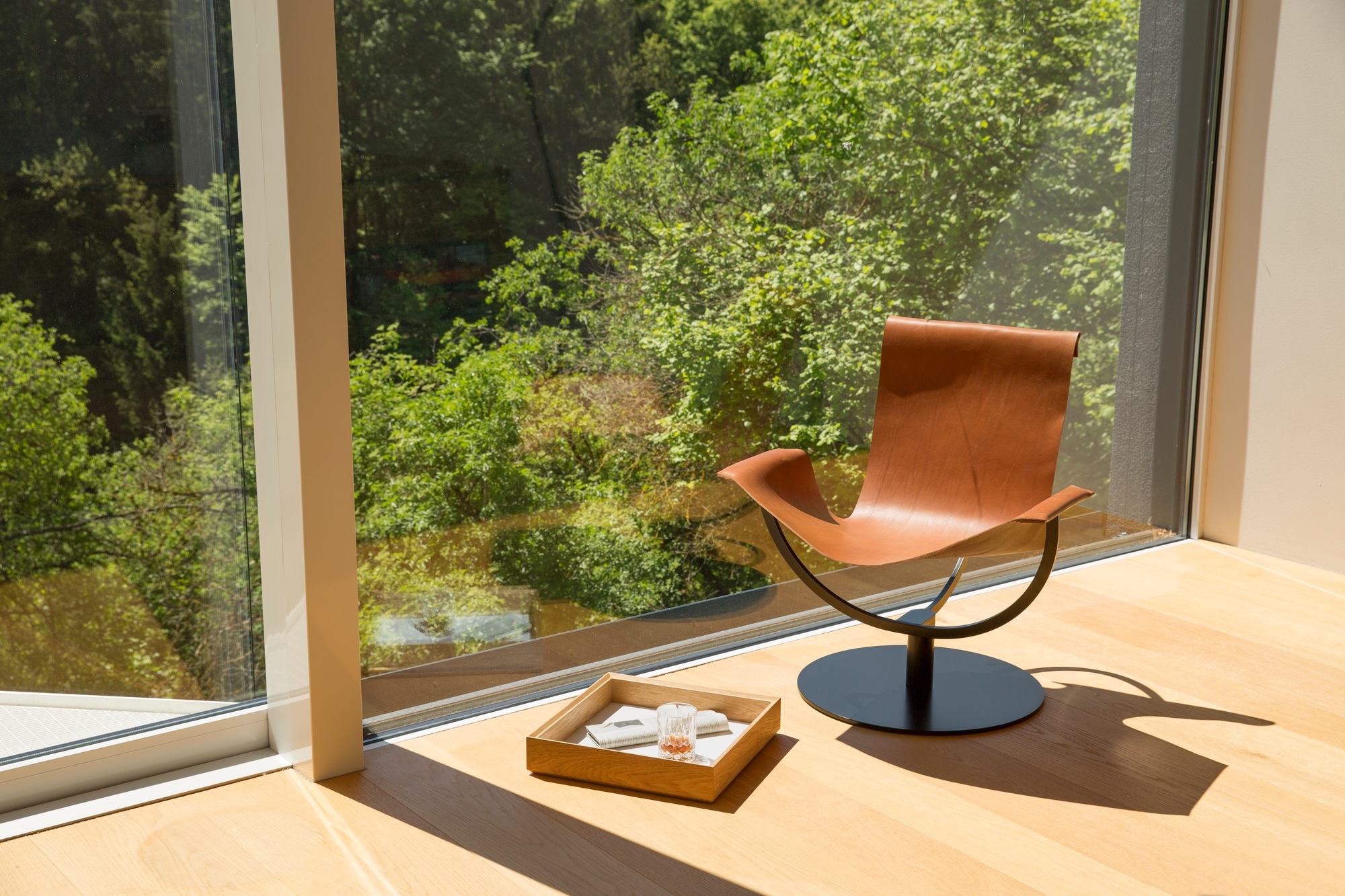 Arch Chair Sessel aus Kernleder in Braun vor Fenster mit Blick ins Grüne.
