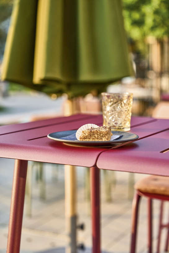 Nahaufnahme des Vapio Hochtisch Outdoor von Weishäupl mit Kuchen und Getränk im Freien.