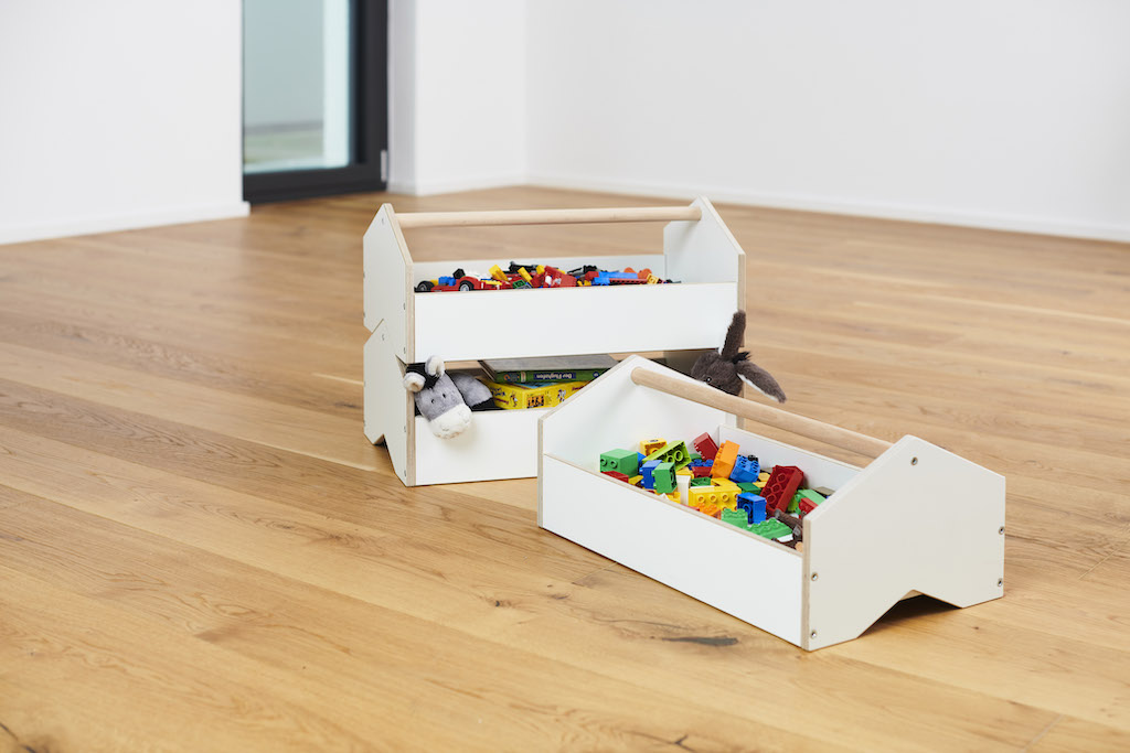 Tojo Kids Werkzeugkiste: Zwei weiße Spielzeugkisten aus Holz, gefüllt mit Spielzeug und Kuscheltieren, auf Holzboden.