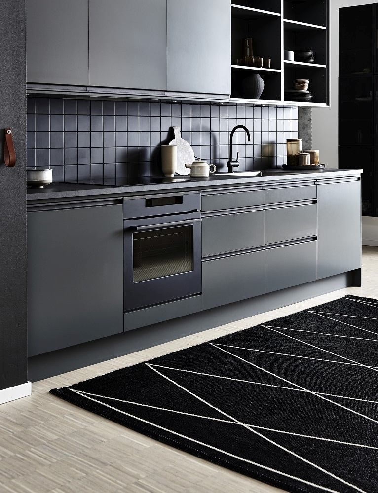 Schwarzer Teppich mit geometrischem Muster in moderner grauer Küche mit Einbaubackofen und schwarzen Fliesen.