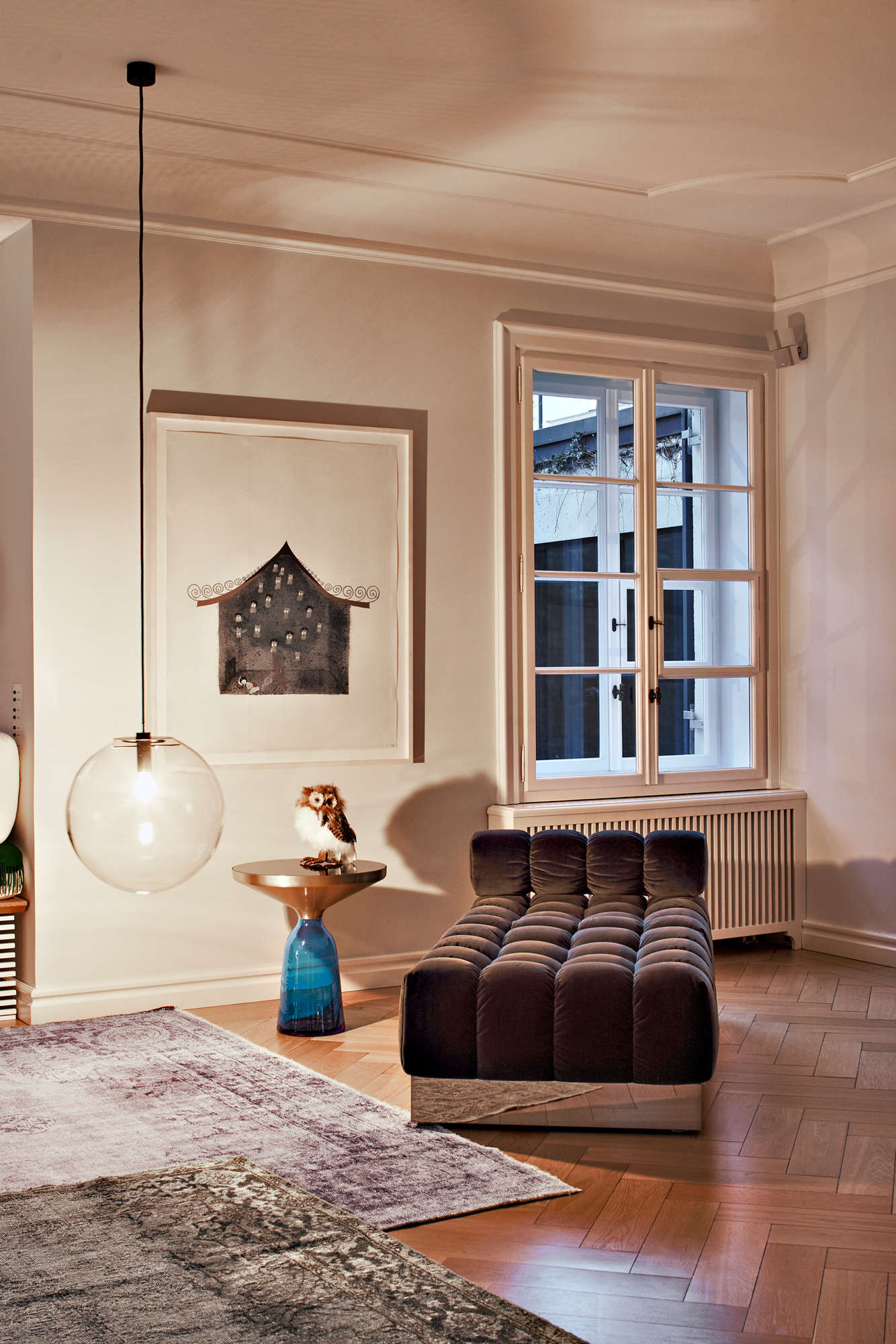 Wohnzimmer-Szene mit ClassiCon Bell Side Table Beistelltisch in Messing mit Dekorationsobjekt Eule, neben einem braunen Sofa.