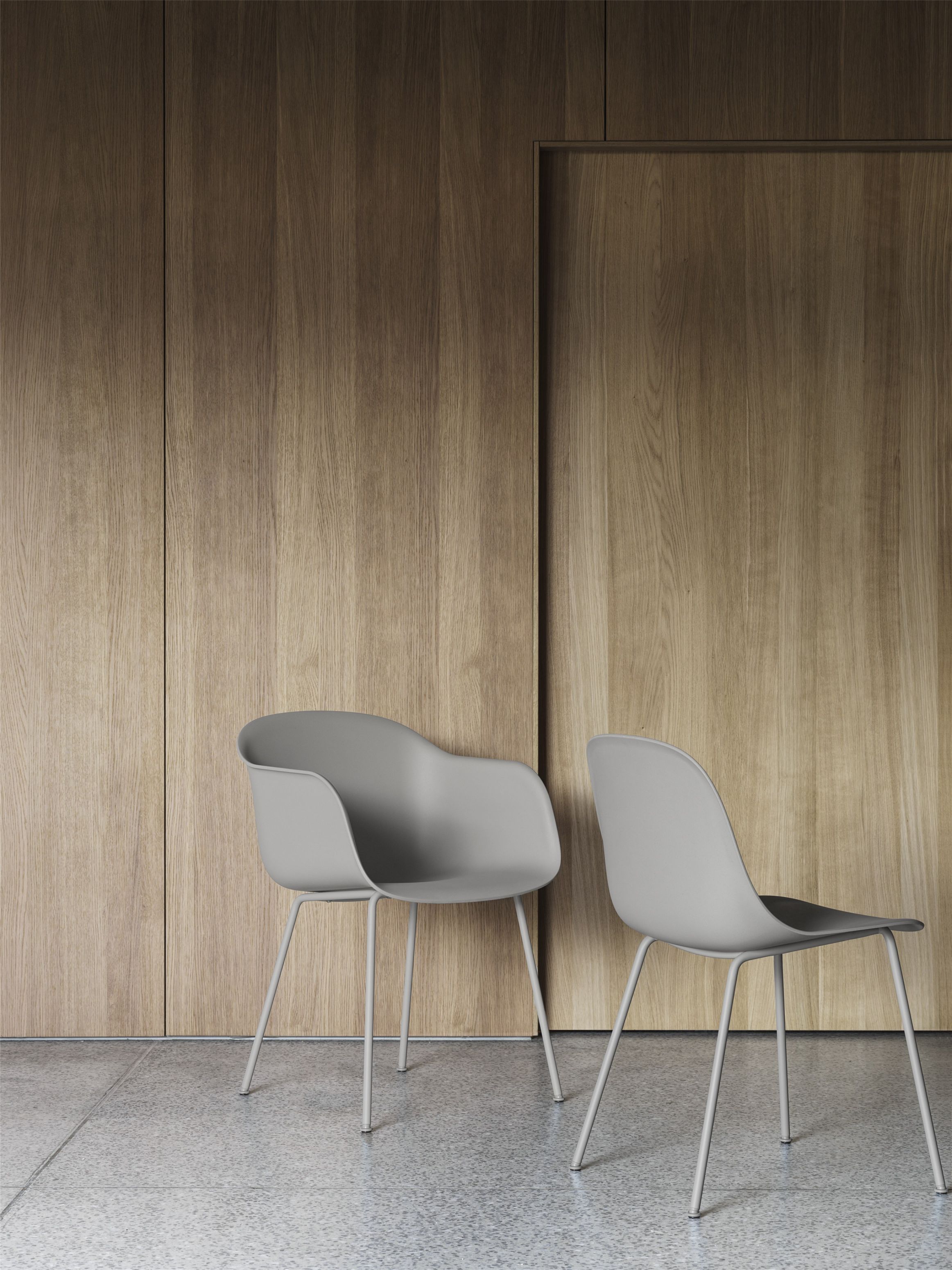 Zwei graue Fiber Armchair Stühle von Muuto mit Stahlrohrgestell vor einer Holzwand.