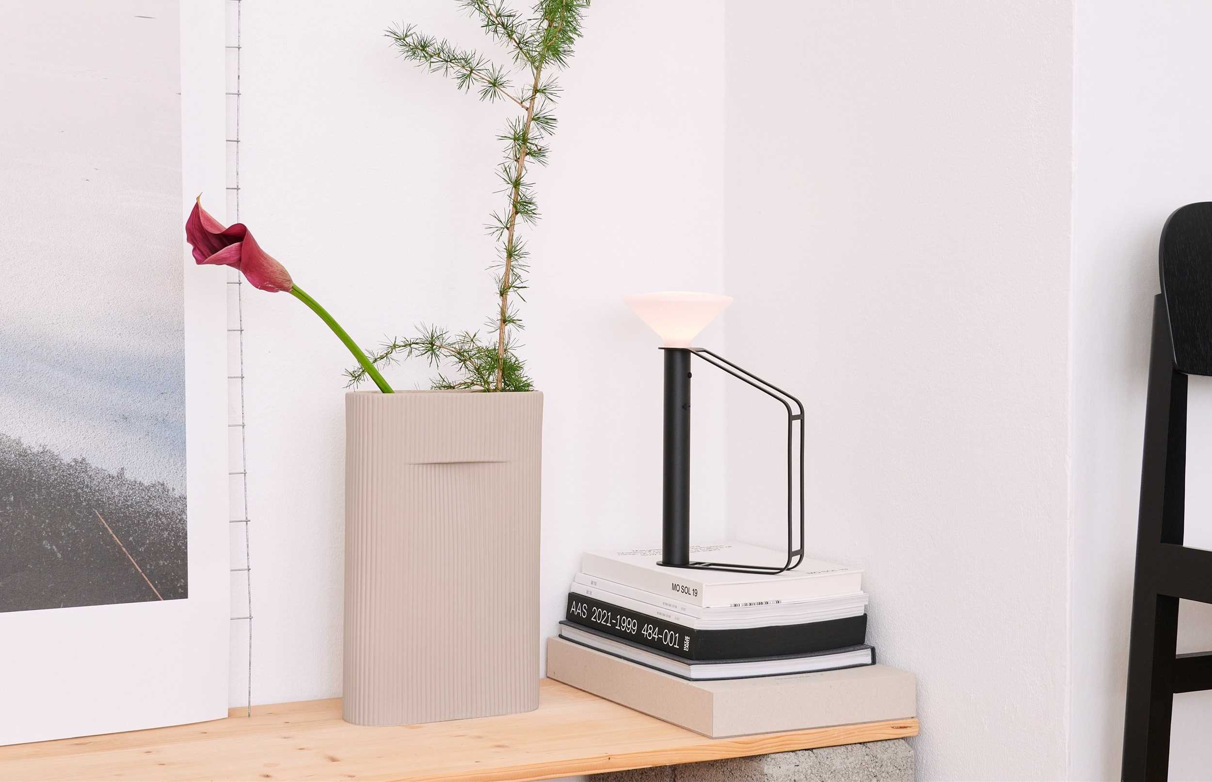 Stillleben mit beiger Design-Vase, moderner schwarzer Tischleuchte und Büchern auf einem Holzregal.