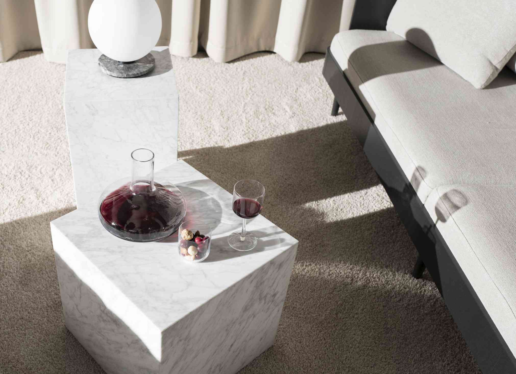 Audo Copenhagen Plinth Tisch aus Marmor mit Dekanter, Weinglas und Süßigkeiten im Wohnzimmer.