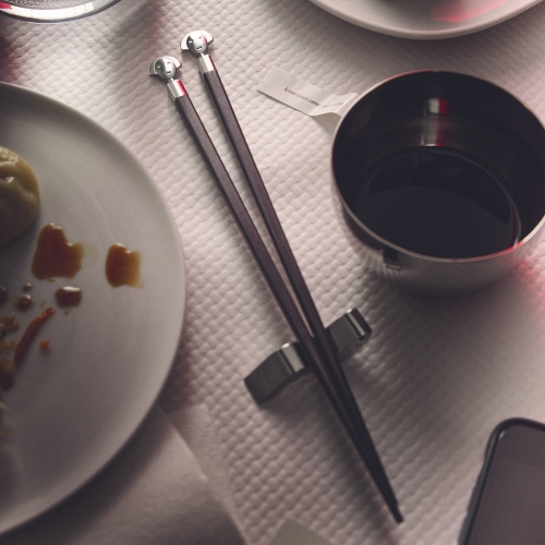 Alessi Anna Stick Essstäbchen Set auf gedecktem Tisch mit Sojasauce und Speisen.