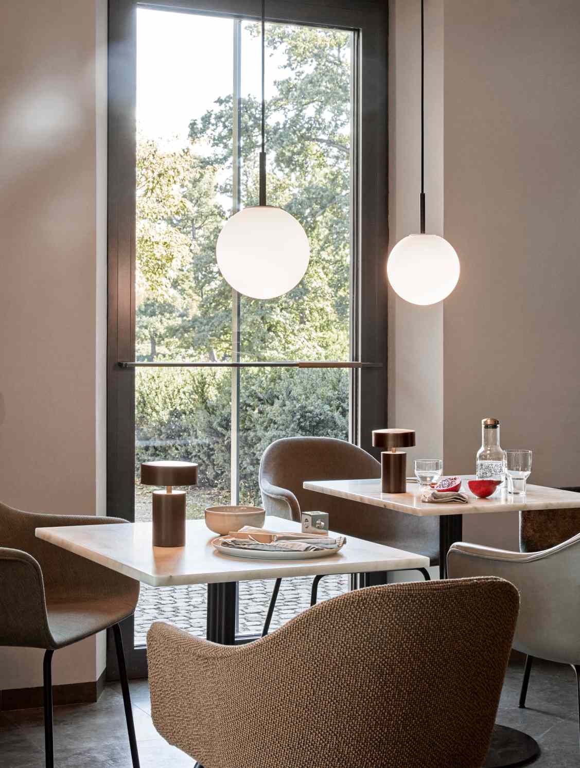 Zwei Audo TR Bulb Pendelleuchten mit Opalglas über Tischen in einem Restaurant.