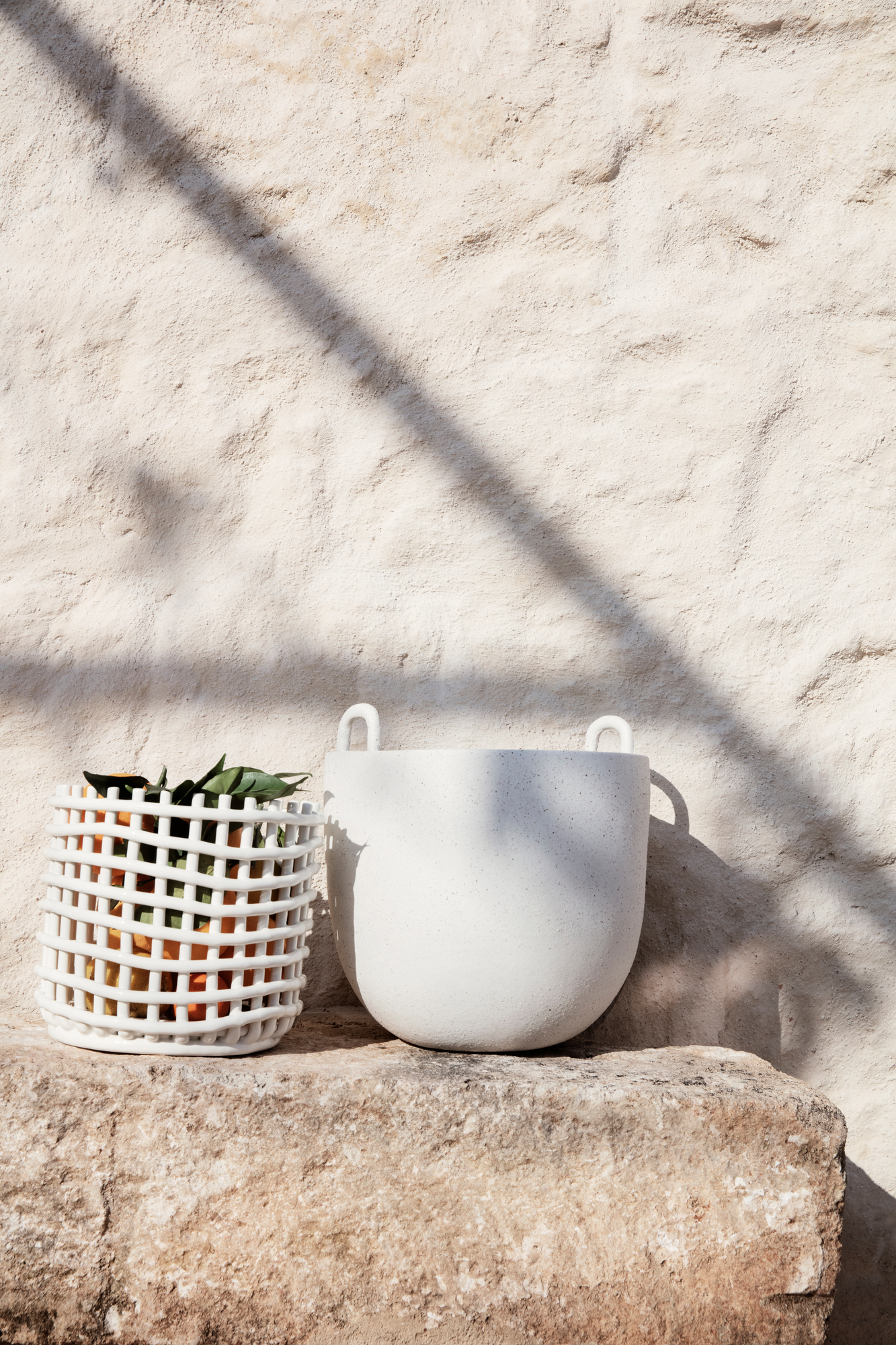 Großer, weißer Keramik Korb von Ferm Living, einer gefüllt mit Orangen, auf Stein.