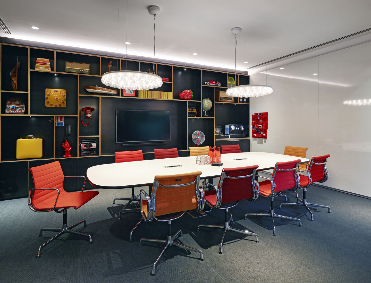 Konferenzraum mit ovalem Tisch und Vitra Aluminium Chair EA 108 Stühlen in Rot und Orange.