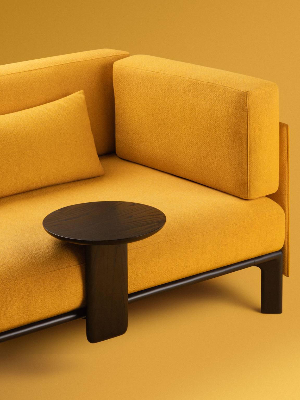 Nahaufnahme des Vitra Anagram Anstecktisches, runde Tischplatte aus dunklem Holz, gelbes Sofa im Hintergrund.