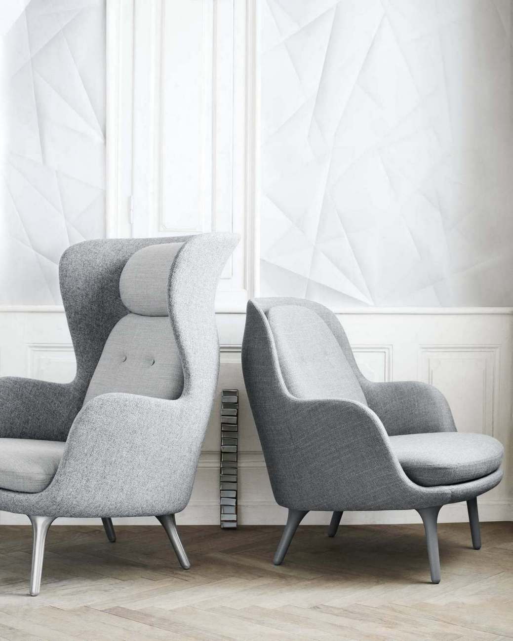 Zwei graue Fri Sessel von Fritz Hansen, ein Ohrensessel und ein Lounge Sessel, vor weißer Wand.